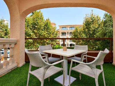 Terras met witte tafel en vier stoelen, omgeven door groene bomen in een hotel.