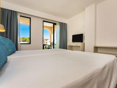 Lichte hotelkamer met tweepersoonsbed, tv en balkon met zeezicht.