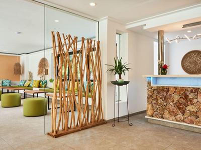 Heldere hotellobby met natuurlijk houten balie, decoratieve planten en zitgedeeltes.