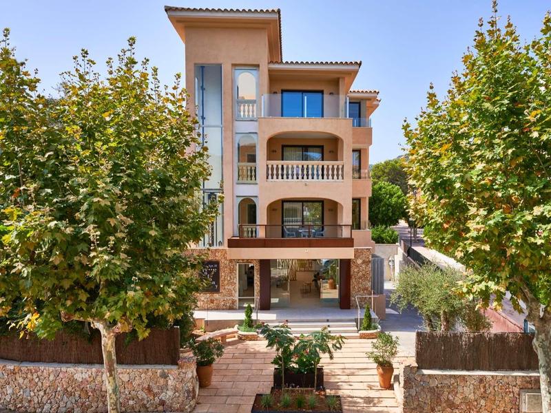 Edificio alberghiero su più piani con balconi, circondato da alberi e da un sentiero curato nel giardino.