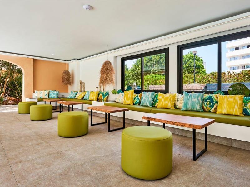 Lounge d'hotel luminosa e moderna con sedute verdi e grandi finestre con vista all'esterno.