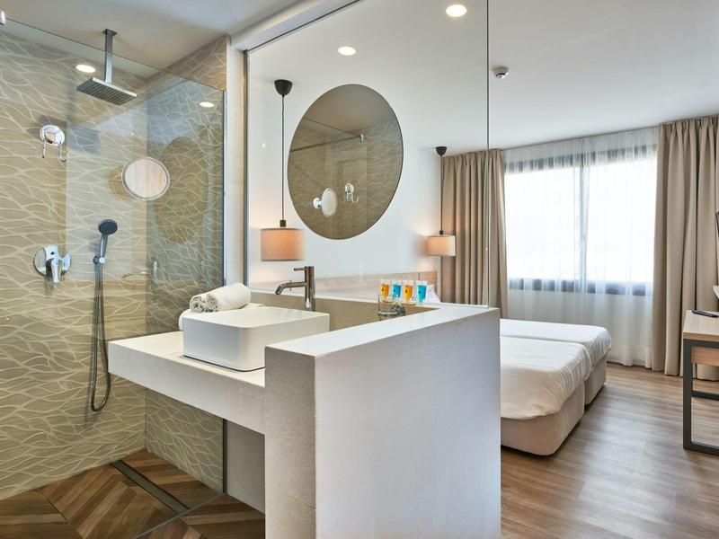 Modern hotelkamer met badkamer, tweepersoonsbed en groot raam met gordijnen.