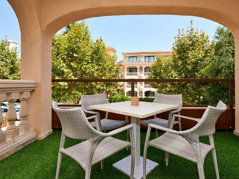 Terras met witte tafel en vier stoelen, omgeven door groene bomen in een hotel.