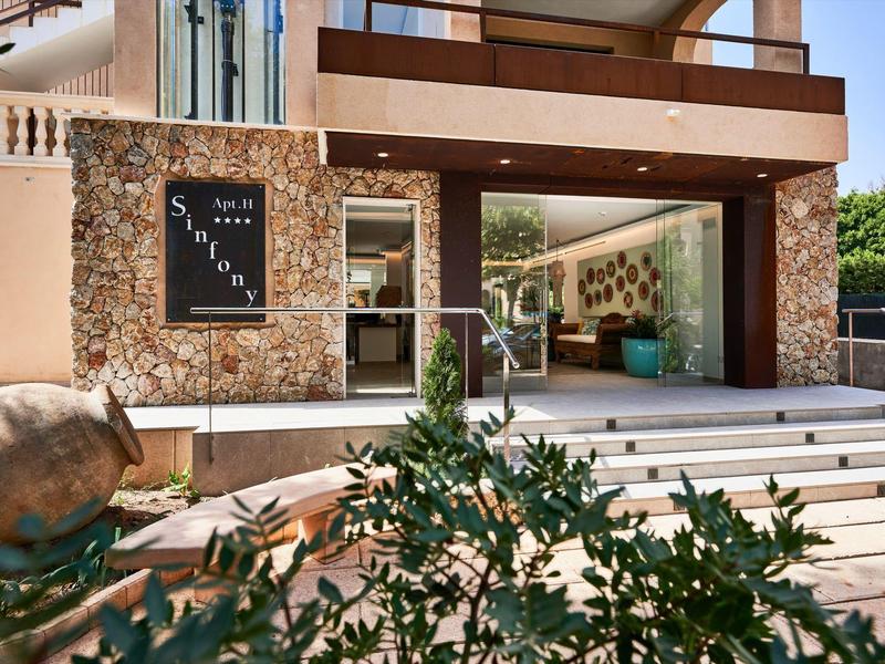 Moderne hotelentree met stenen trap en glazen gevel, geflankeerd door planten en een sculptuur.