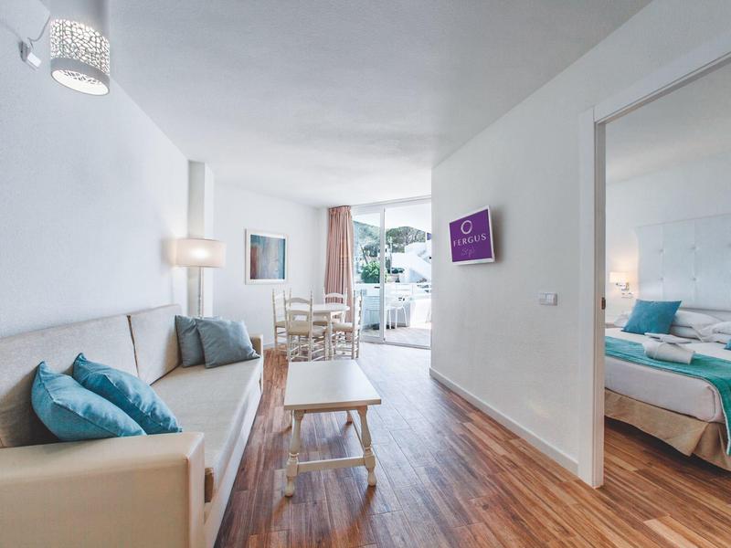 Světý obývací pokoj s pohovkou, konferenčním stolkem a sousední ložnicí s manželskou postelí.