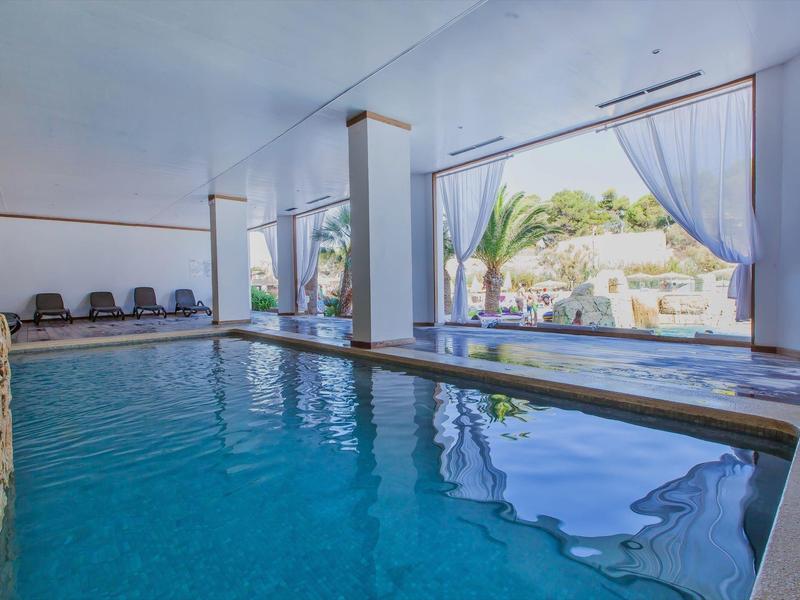 Vnitřní bazén s velkými okny s výhledem na zahradu a lehátka.