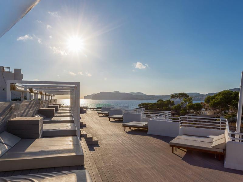 Slunná terasa s lehátky a výhledem na moře a vzdálené ostrovy.