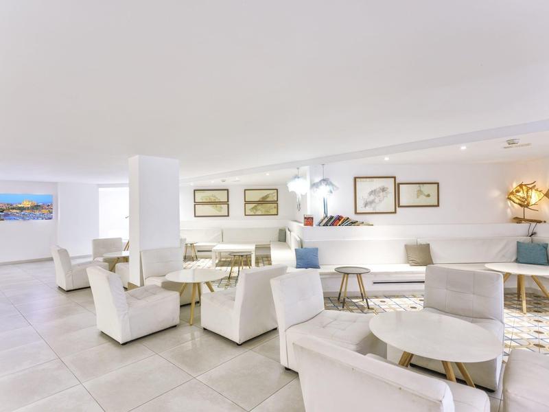 Světlý salonek s bílými křesly, kulatými stoly, stěnami s rámy a květinovou dekorací.