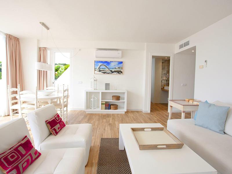 Světlý obývací pokoj s bílými pohovkami, barevnými polštáři, moderním zařízením a velkým oknem.