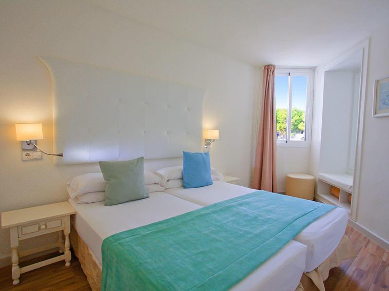 Světlo hotelový pokoj s manželskou postelí a jednoduchým bílomodrým zařízením.