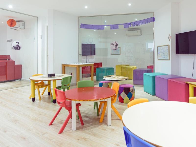 Barevná herna s dětskými stolky a židlemi v moderním interiéru.