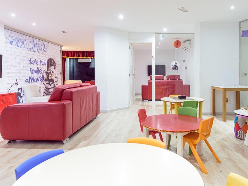Barevná odpočinková místnost s červenými pohovkami a vícebarevnými dětskými stolky.