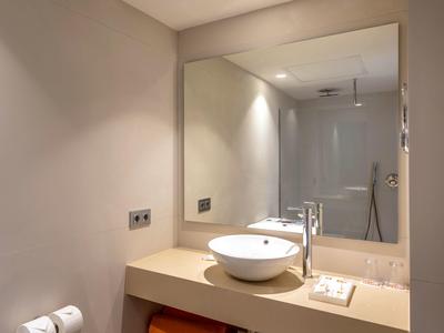 Moderne Badezimmer mit rundem Waschbecken, großer Spiegel und Badewanne im Hintergrund.