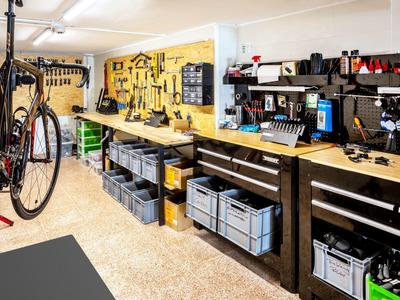 Werkstatt mit Fahrrad, Werkzeugwand, Werkbänken und Lagerboxen, helle Beleuchtung und geordnete Ausstattung.