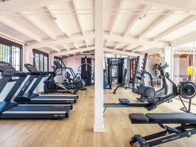 Hell beleuchteter Fitnessraum mit Laufbändern, Fahrrädern und verschiedenen Trainingsgeräten.