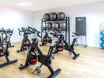 Fitnessraum mit mehreren schwarzen Spinning-Bikes, Gymnastikbällen und Hantelscheiben an der Wand.