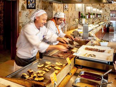 Zwei Köche bereiten viele kleine Speisen an einer langen Buffet-Theke zu.