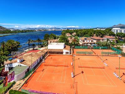 Mehrere rote Tennisplätze und ein Fluss mit Bergen im Hintergrund unter klarem blauem Himmel.