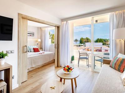 Helles Wohnzimmer mit Sofa, Couchtisch und Balkon, angrenzendes Schlafzimmer mit Tagesbett.