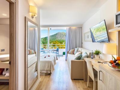 Helles, modernes Hotelzimmer mit Balkon, Sitzbereich, Doppelbett und Blick auf grüne Berge.