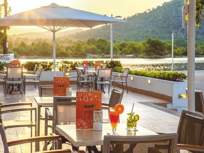 Restaurantterrasse mit Tischen, Stühlen, Sonnenschirmen und Getränken bei Sonnenuntergang.