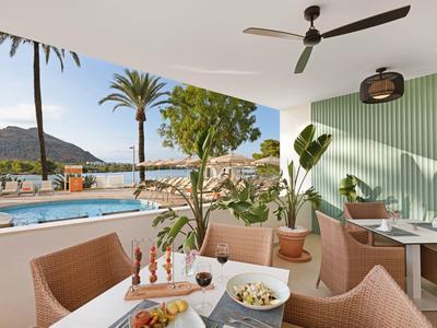 Terrasse mit Tisch, Stühlen und Deckenventilator, Pool, Palmen und Bergen im Hintergrund.