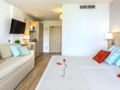 Modernes Hotelzimmer mit Doppelbett, Sofa, Holzfußboden und neutraler Farbgestaltung.
