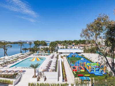 Strandhotel mit Sonnenschirmen, Liegestühlen und einem bunten Kinderspielplatz am Meer.