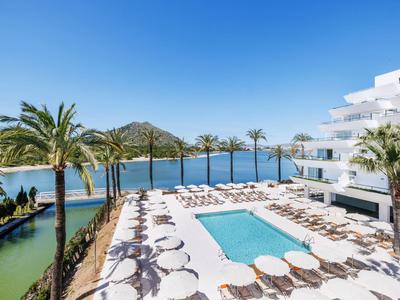 Moderner Hotelpool mit weißen Liegen, umgeben von Palmen, mit Blick auf das Meer und Berge.