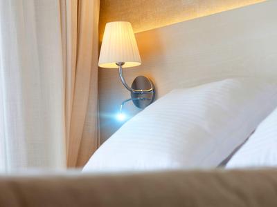 Beleuchtete Wandlampe neben weißen Kissen an einem hellen Kopfteil im Schlafzimmer.
