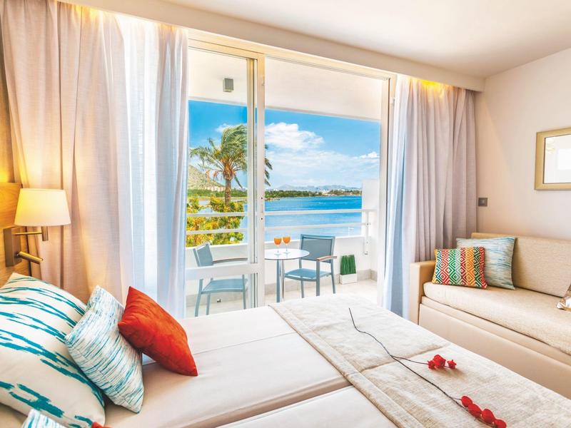 Helles Hotelzimmer mit Doppelbett und Balkon mit Meerblick bei Tageslicht.