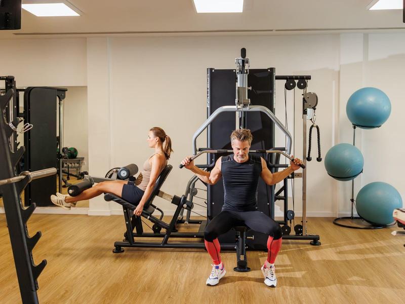 Zwei junge Männer trainieren Kraftübungen an Fitnessgeräten in einem modernen Fitnessstudio.