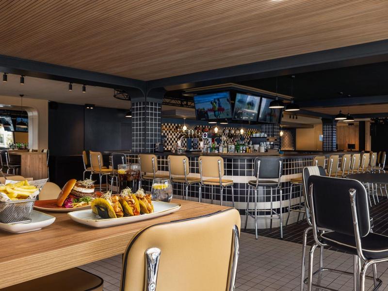 Moderner Hotelbarbereich mit Holztisch, bequemen Stühlen und einem Tresen mit Barhockern.