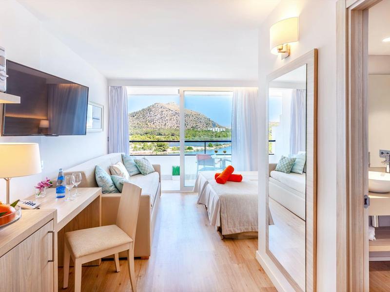 Helles Hotelzimmer mit Blick auf das Meer und einen Berg, moderner Einrichtung und Badezimmer.