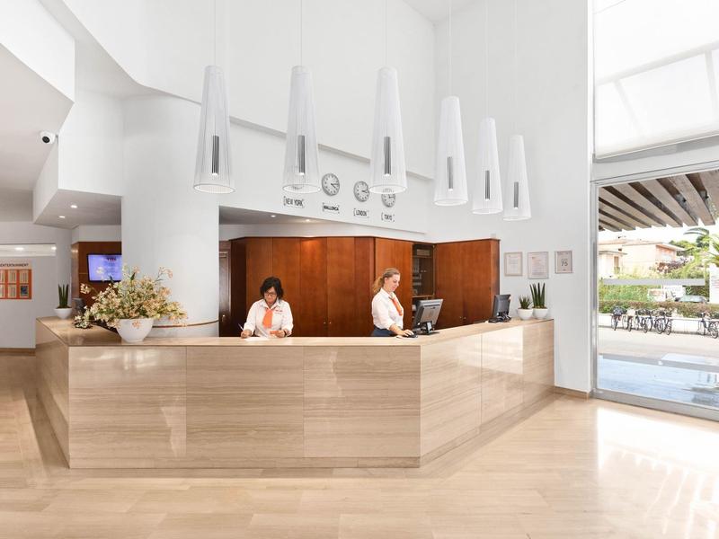 Moderner Hotelempfang mit hellem Holz, Rezeptionisten und Blick auf den Außenpool.