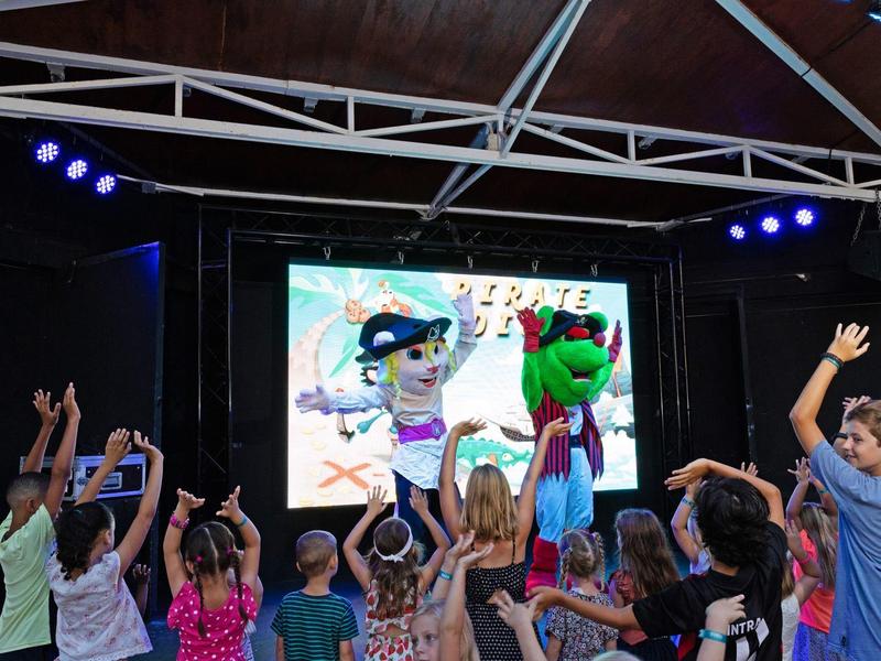 Kinder stehen vor einer Bühne mit zwei Kostümpuppen im Freien bei einer Veranstaltung.