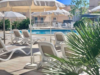 Poolbereich mit weißen Liegestühlen und Sonnenschirmen neben einem Hotelgebäude