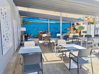 Buiten eetgedeelte met witte tafels en stoelen onder een overdekt terras met een blauwe muurschildering.