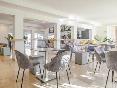 Lichte, moderne eetruimte met grijze stoelen, glazen tafels en kamerplanten bij grote ramen.