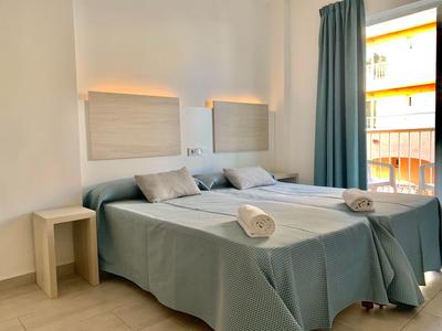 Een eenvoudige hotelkamer met twee bedden, grijze bedspreien en een klein houten tafeltje.