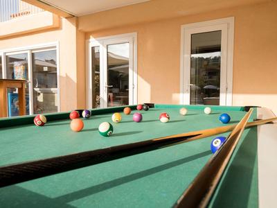 Ein grüner Billardtisch mit bunten Kugeln in einem sonnendurchfluteten Raum mit orangefarbenen Wänden.