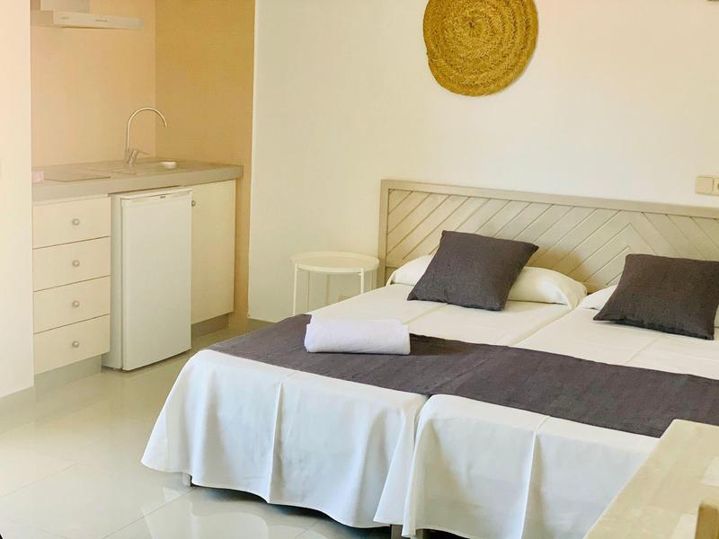 Lichte hotelkamer met tweepersoonsbed, kleine koelkast en kitchenette.