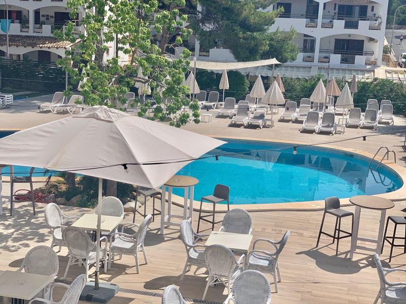 Buitenzwembad met witte stoelen en tafels onder grote parasols naast een blauw rond zwembad.