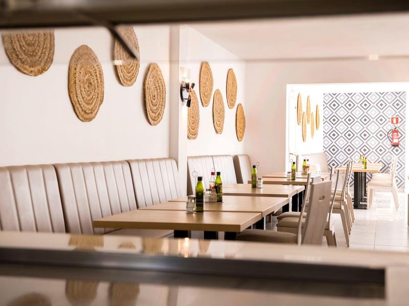 Lichte restaurantruimte met houten tafels, beklede banken en geweven wanddecoraties.