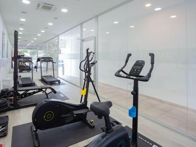Moderner Fitnessraum mit Cardio-Geräten auf hellem Boden und weißen Wänden, gut beleuchtet.