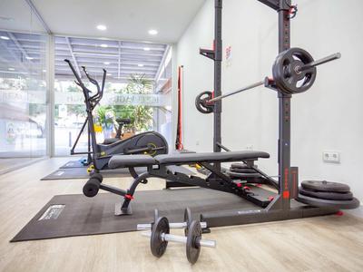 Moderner Fitnessraum mit Hantelbank, Ellipsentrainer und Kurzhanteln auf heller Holzfläche.