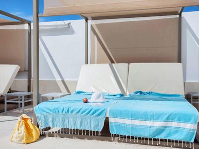 Zwei weiße Liegen mit blauen Handtüchern auf einer Terrasse unter Sonnenschutz.