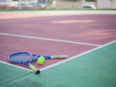 Tennisplatz mit grünem und rotem Belag, blauem Tennisschläger und gelbem Ball am Netzrand.