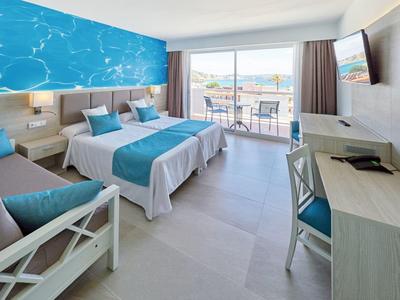 Helles Hotelzimmer mit Doppelbett, blau-weißer Bettwäsche, Terrasse und Meerblick.