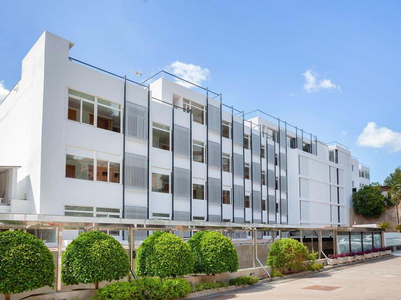 Modern white hotel building with many windows and a neat front garden on a sunny day.